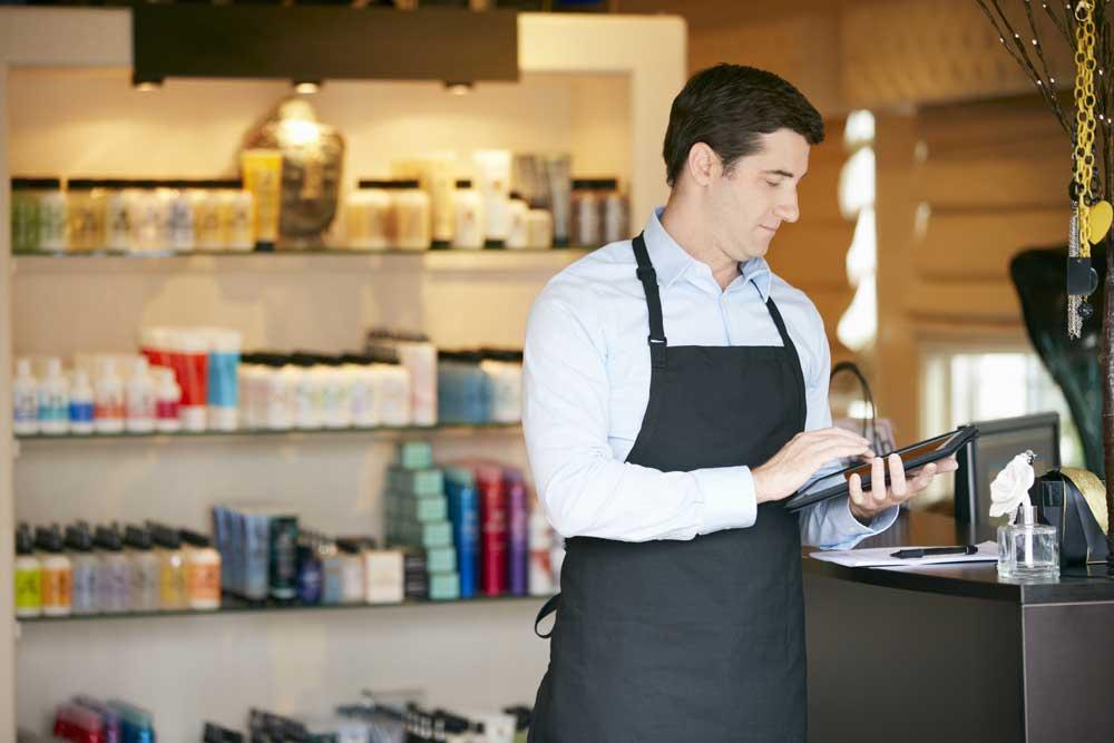 Verkäufer mit Schürze im Geschäft mit Tablet vor einem Verkaufsregal